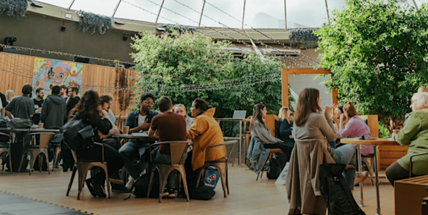 Image of people sat around tables, talking, with trees around