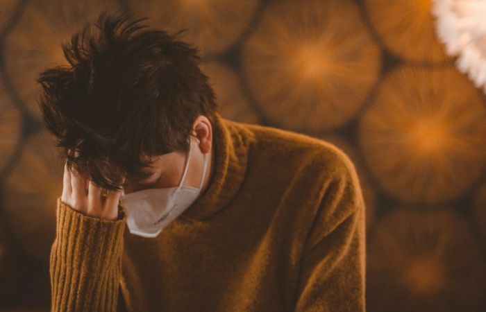Man with face mask rests his head on one hand in despair