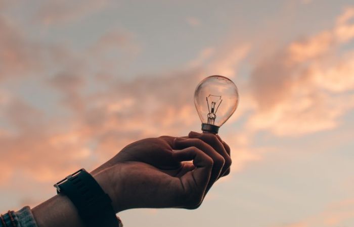 Hand holding lightbulb with sky as background