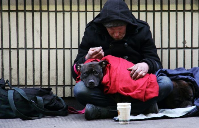 Homeless man with dog on lap sitting on a pavement