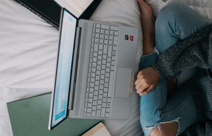Aerial view of female sitting on a bed surrounded by a diary, books and a laptop
